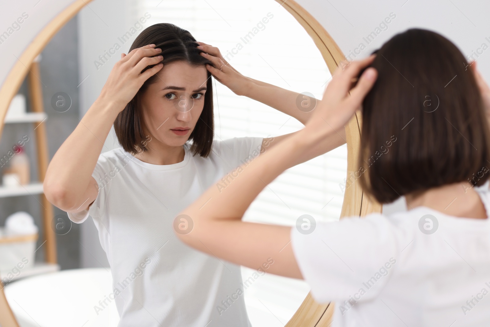 Photo of Sad woman with hair loss problem looking at mirror indoors