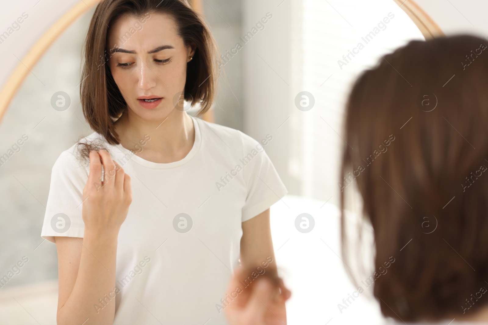 Photo of Stressed woman holding clump of lost hair near mirror indoors. Alopecia problem
