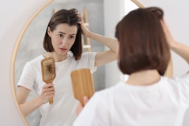 Sad woman holding brush with lost hair indoors. Alopecia problem