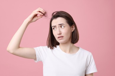 Young woman suffering from hair loss problem on pink background