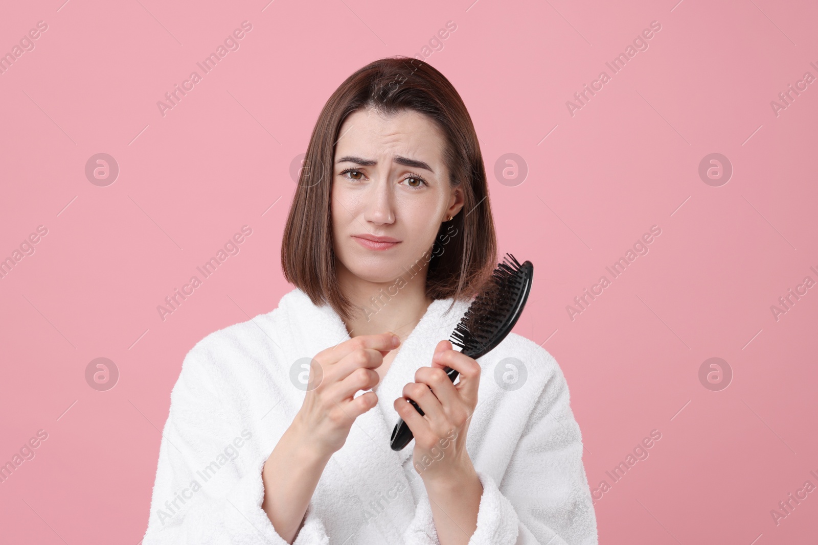 Photo of Sad woman holding brush with lost hair on pink background. Alopecia problem