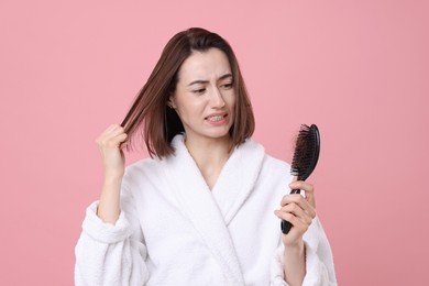 Emotional woman holding brush with lost hair on pink background. Alopecia problem