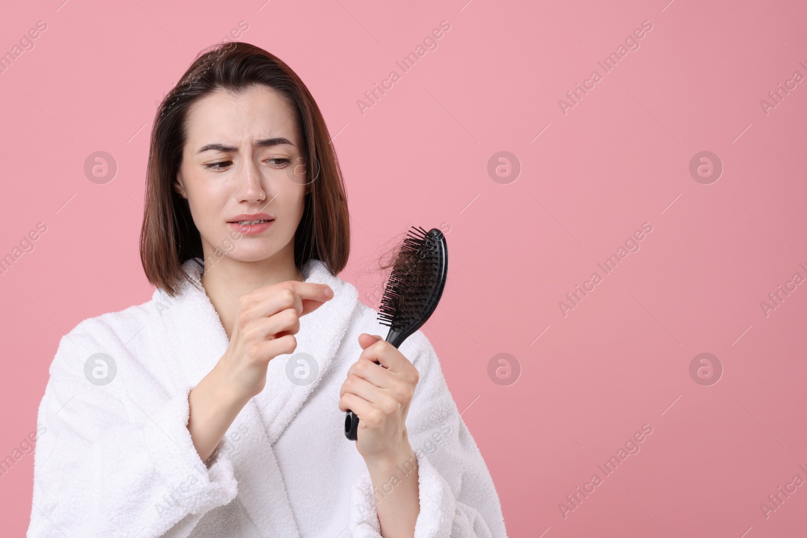 Photo of Stressed woman taking her lost hair from brush on pink background, space for text. Alopecia problem