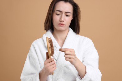 Sad woman taking her lost hair from brush on light brown background. Alopecia problem