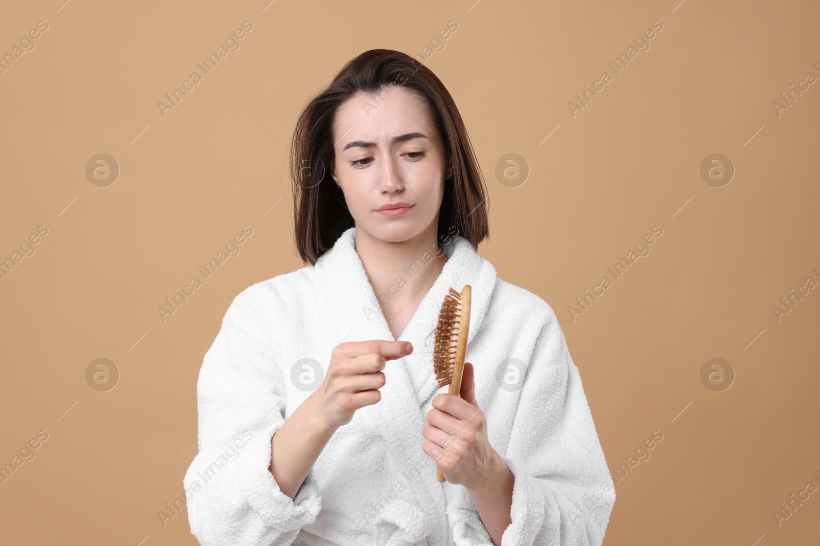 Photo of Sad woman taking her lost hair from brush on light brown background. Alopecia problem