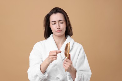 Sad woman taking her lost hair from brush on light brown background. Alopecia problem