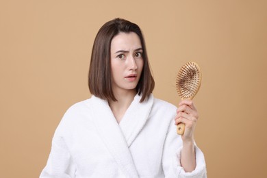 Photo of Stressed woman holding brush with lost hair on light brown background. Alopecia problem