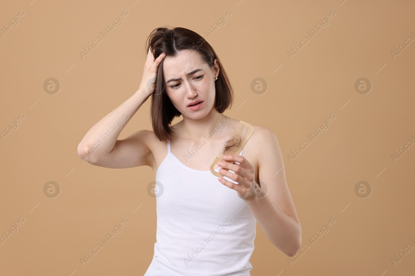 Photo of Stressed woman holding comb with lost hair on light brown background. Alopecia problem