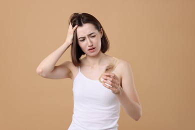 Photo of Stressed woman holding comb with lost hair on light brown background. Alopecia problem