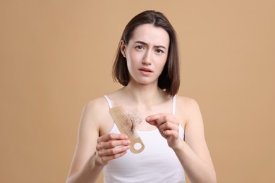 Sad woman taking her lost hair from comb on light brown background. Alopecia problem