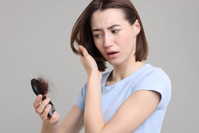 Stressed woman holding brush with lost hair on grey background. Alopecia problem