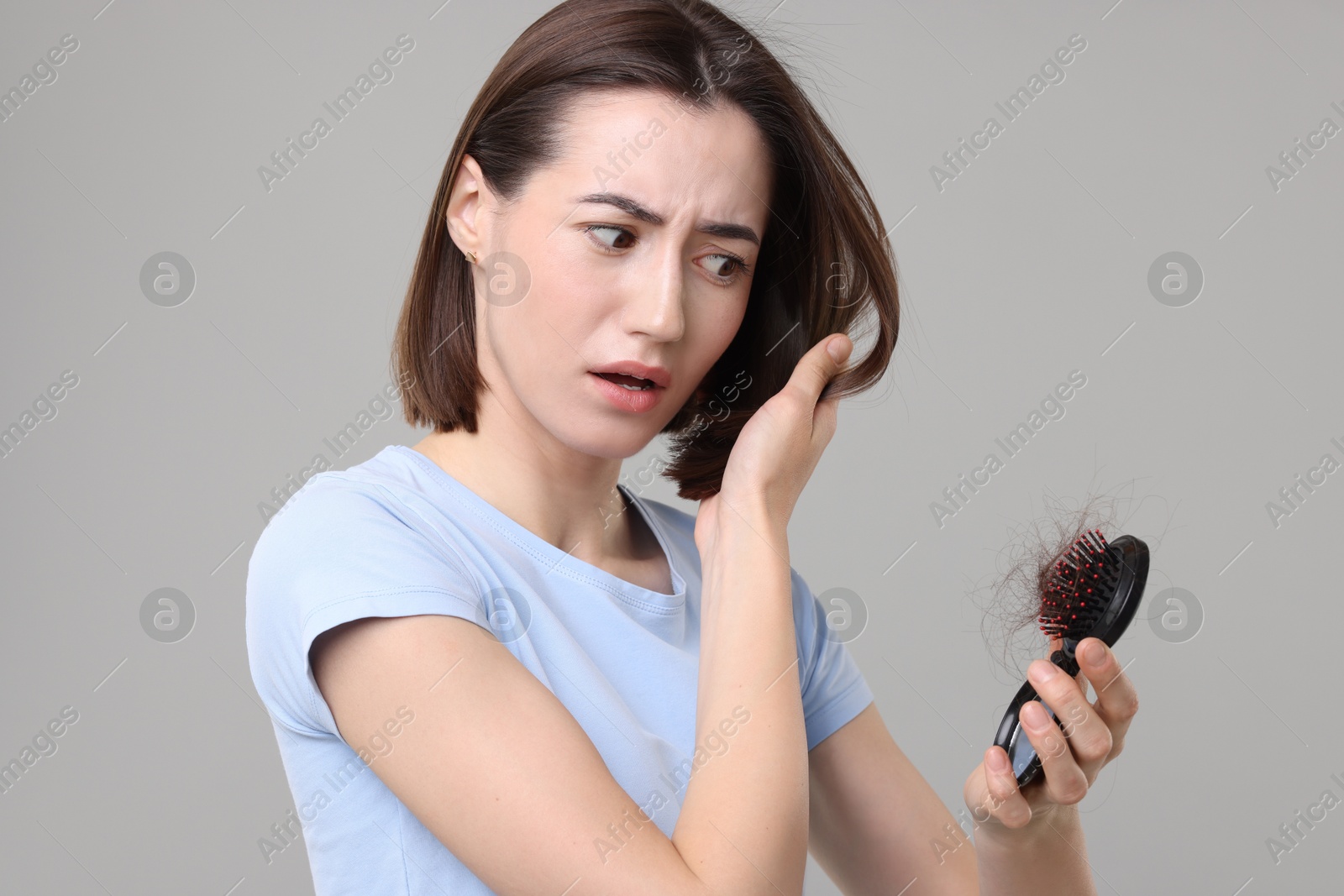 Photo of Stressed woman holding brush with lost hair on grey background. Alopecia problem