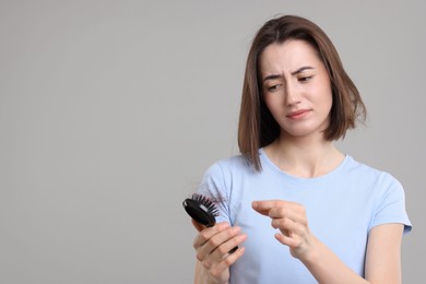 Sad woman taking her lost hair from brush on grey background, space for text. Alopecia problem