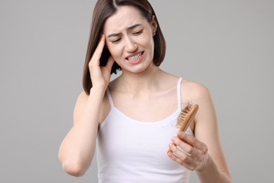 Emotional woman holding brush with lost hair on grey background. Alopecia problem