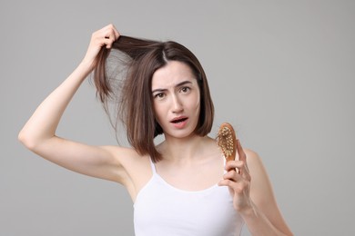 Emotional woman holding brush with lost hair on grey background. Alopecia problem