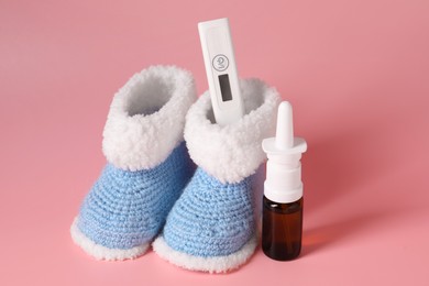 Photo of Baby`s booties, thermometer and nasal spray on pink background