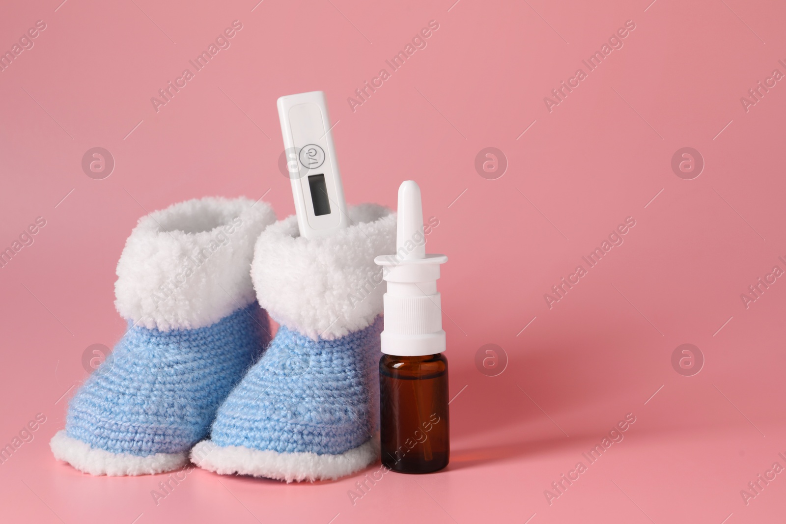 Photo of Baby`s booties, thermometer and nasal spray on pink background, space for text