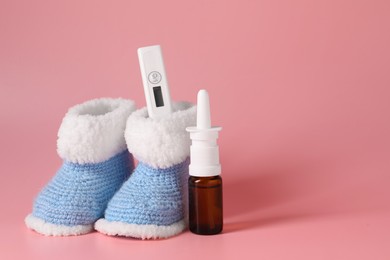 Baby`s booties, thermometer and nasal spray on pink background, space for text