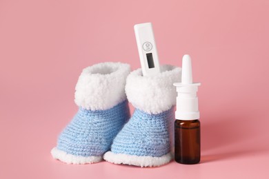 Photo of Baby`s booties, thermometer and nasal spray on pink background