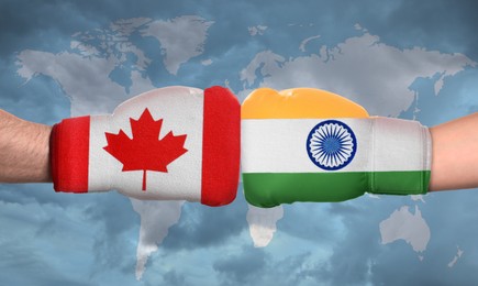 Political conflict. Men in boxing gloves with flags of Canada and India fighting against world map, closeup