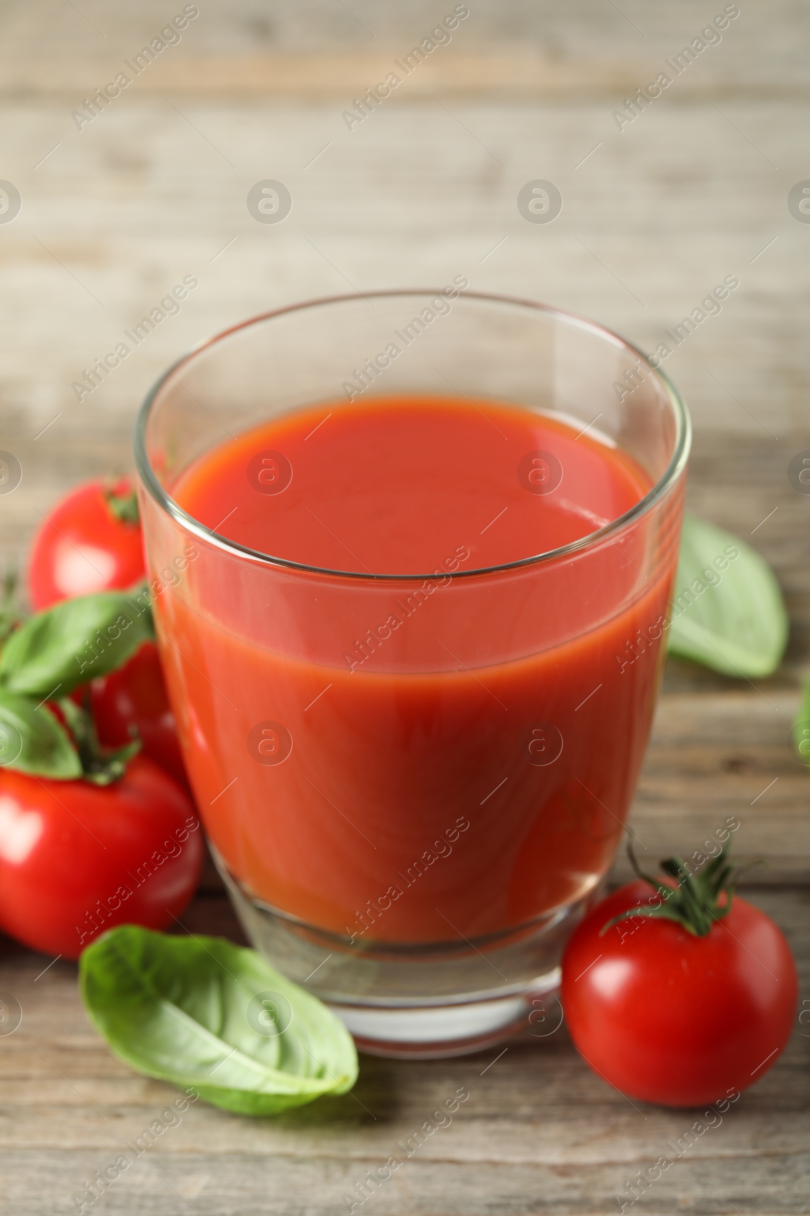 Photo of Tasty tomato juice in glass, basil leaves and fresh vegetables on wooden table, closeup