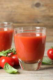 Photo of Tasty tomato juice in glasses, basil leaves and fresh vegetables on wooden table, closeup