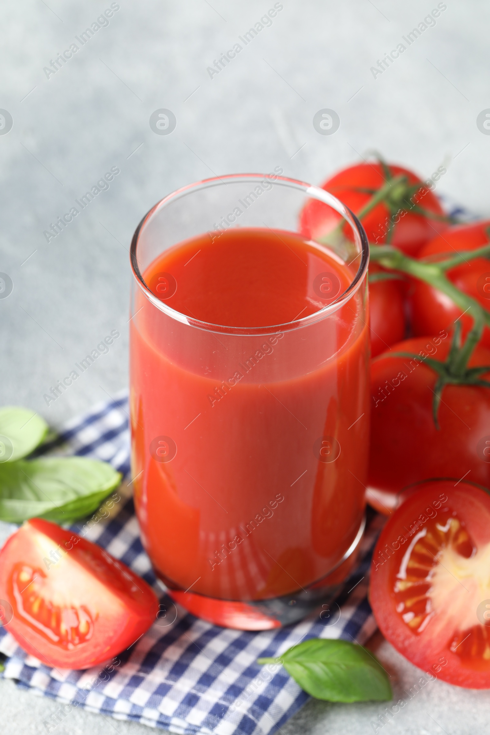 Photo of Tasty tomato juice in glass, basil leaves and fresh vegetables on grey table