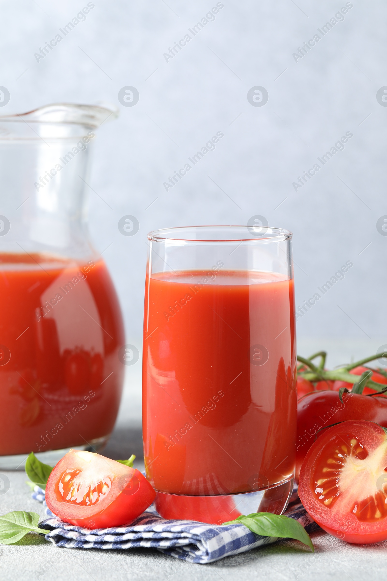 Photo of Tasty tomato juice with fresh vegetables and basil leaves on light grey table