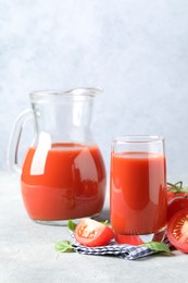 Photo of Tasty tomato juice with fresh vegetables and basil leaves on light grey table