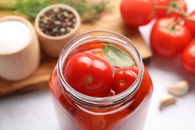 Photo of Tasty pickled tomatoes in jar, fresh vegetables and spices on table, closeup