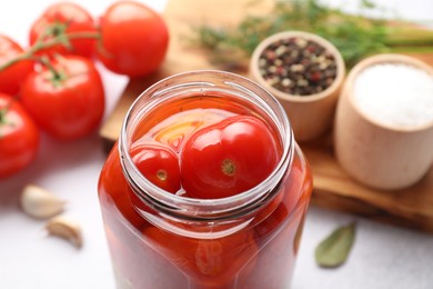 Tasty pickled tomatoes in jar, fresh vegetables and spices on table, closeup