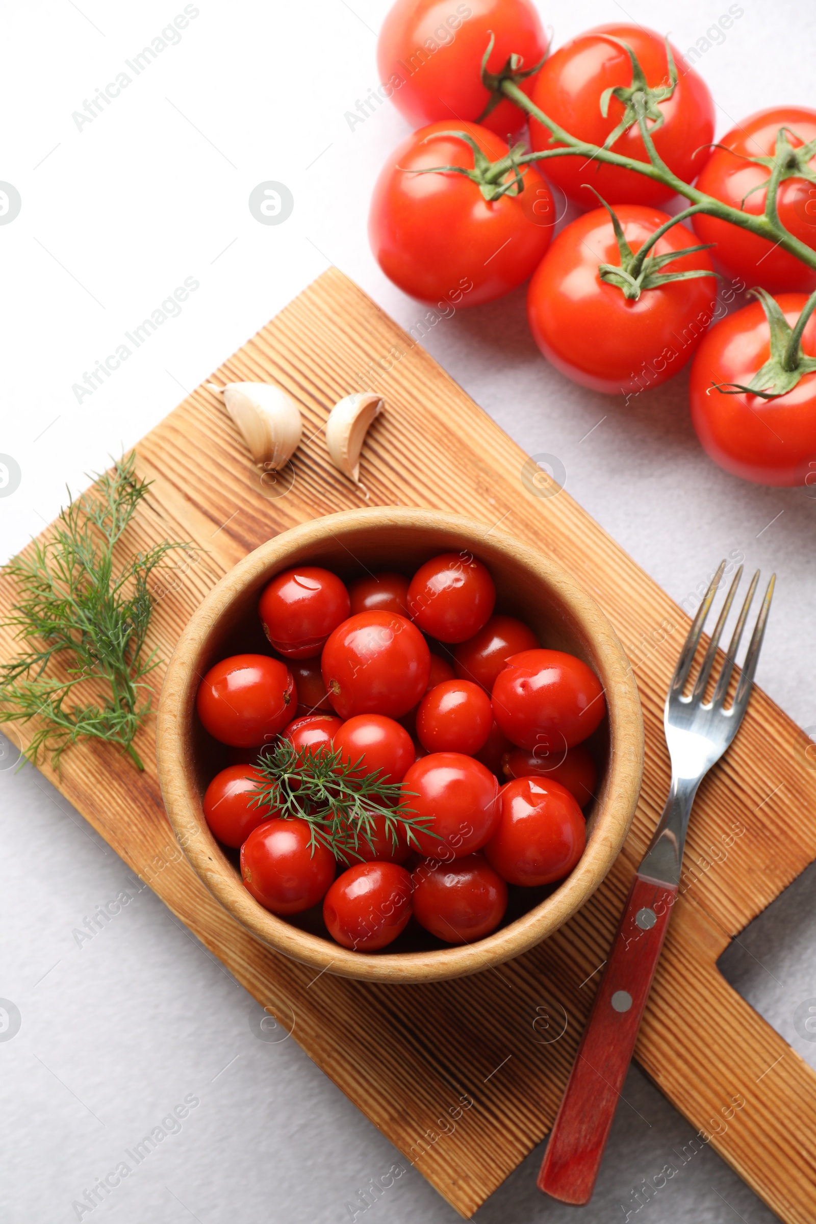 Photo of Tasty pickled tomatoes in bowl, fresh vegetables, dill, garlic and fork on white table, top view