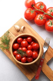 Photo of Tasty pickled tomatoes in bowl, fresh vegetables, dill, garlic and fork on white table, top view
