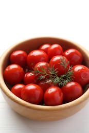 Tasty pickled tomatoes and dill in bowl on white wooden table
