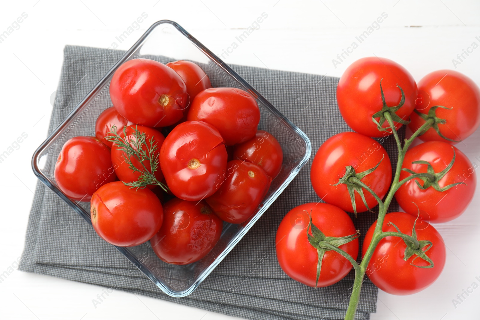 Photo of Tasty pickled tomatoes in bowl, fresh vegetables and fork on white table, top view