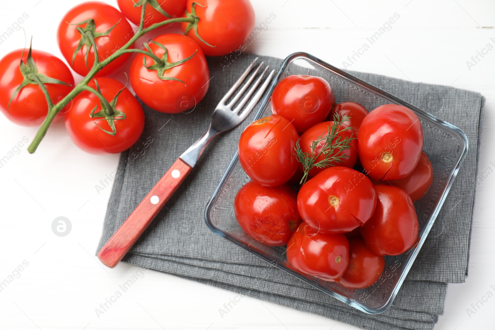 Photo of Tasty pickled tomatoes in bowl, fresh vegetables and fork on white table, top view