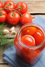 Tasty pickled tomatoes in jar, spices and fresh vegetables on wooden table