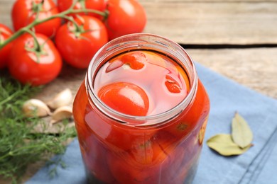 Tasty pickled tomatoes in jar, spices and fresh vegetables on wooden table, closeup
