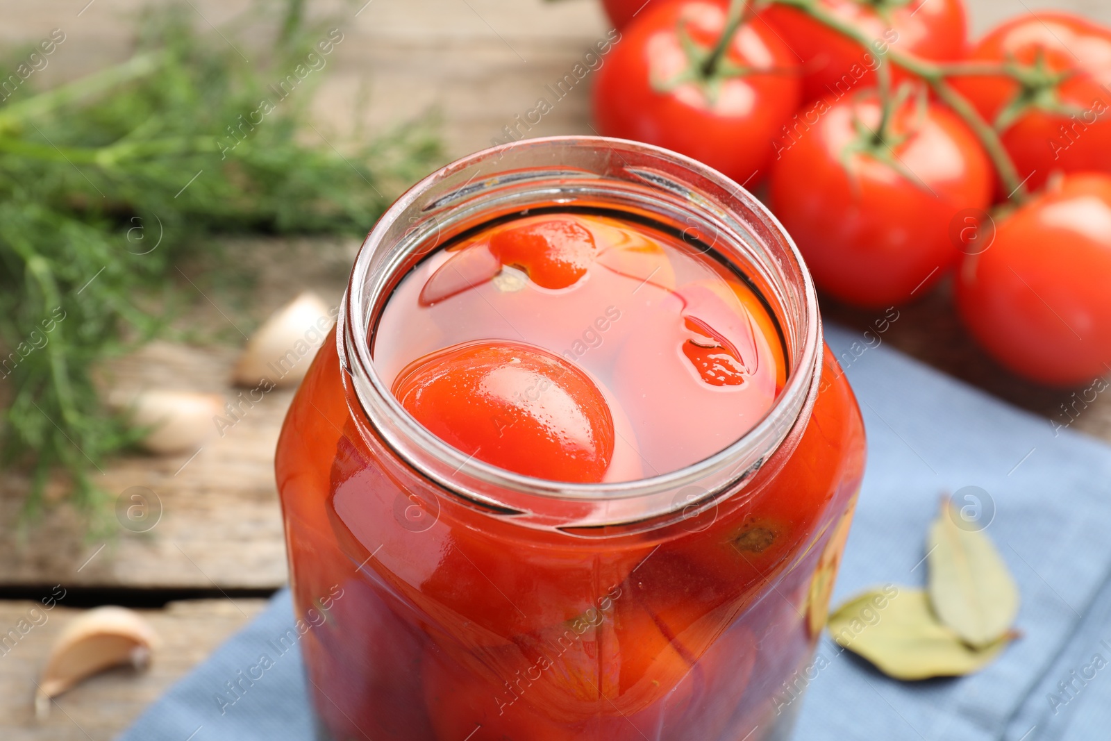 Photo of Tasty pickled tomatoes in jar, spices and fresh vegetables on wooden table, closeup