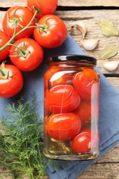 Tasty pickled tomatoes in jar, spices and fresh vegetables on wooden table, top view