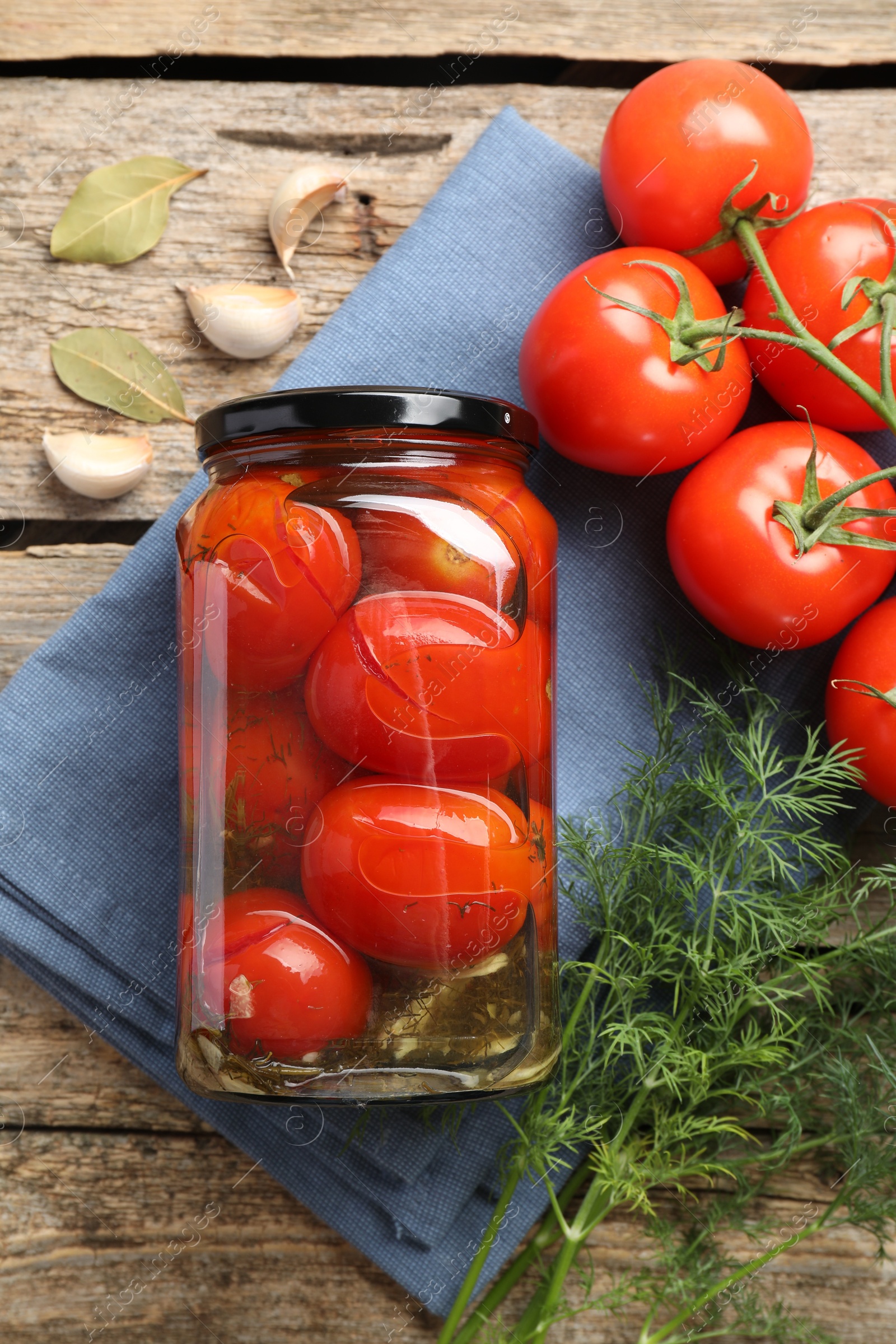 Photo of Tasty pickled tomatoes in jar, spices and fresh vegetables on wooden table, top view