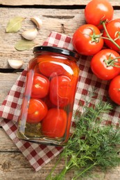 Tasty pickled tomatoes in jar, spices and fresh vegetables on wooden table, top view