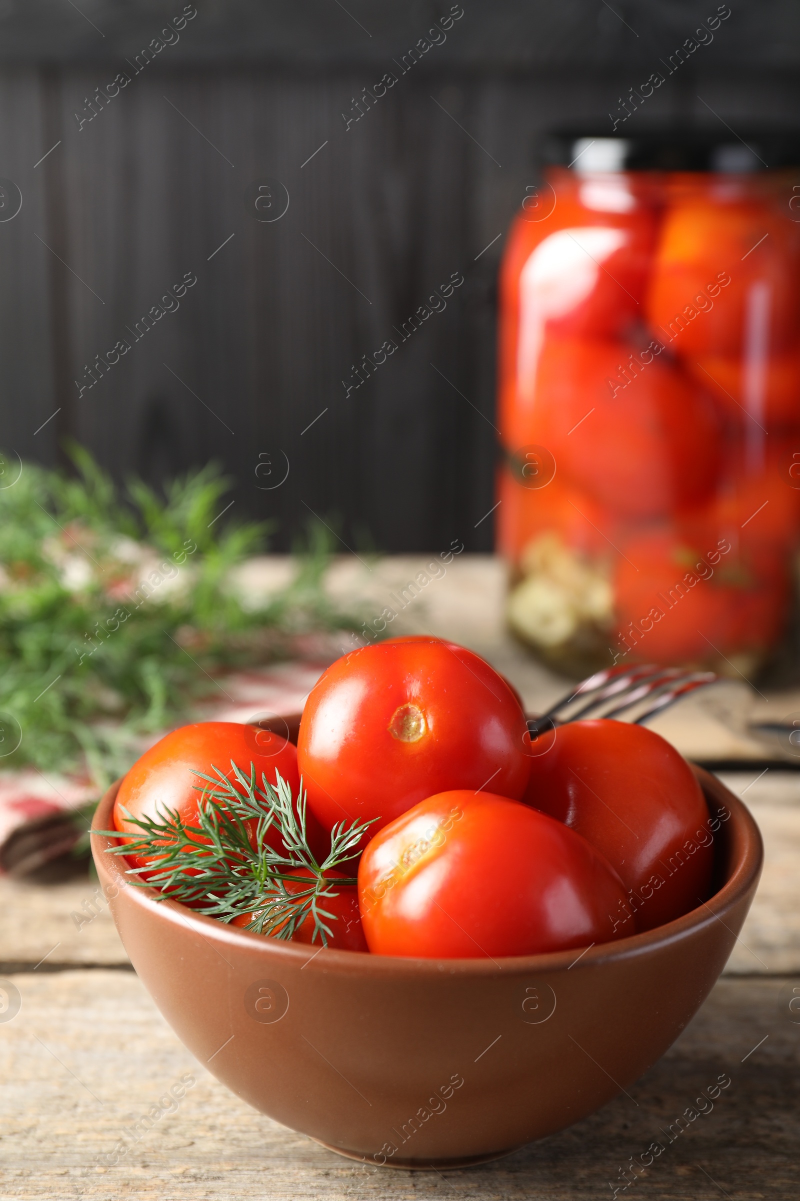 Photo of Tasty pickled tomatoes, dill and fork on wooden table