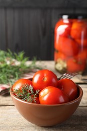Tasty pickled tomatoes, dill and fork on wooden table