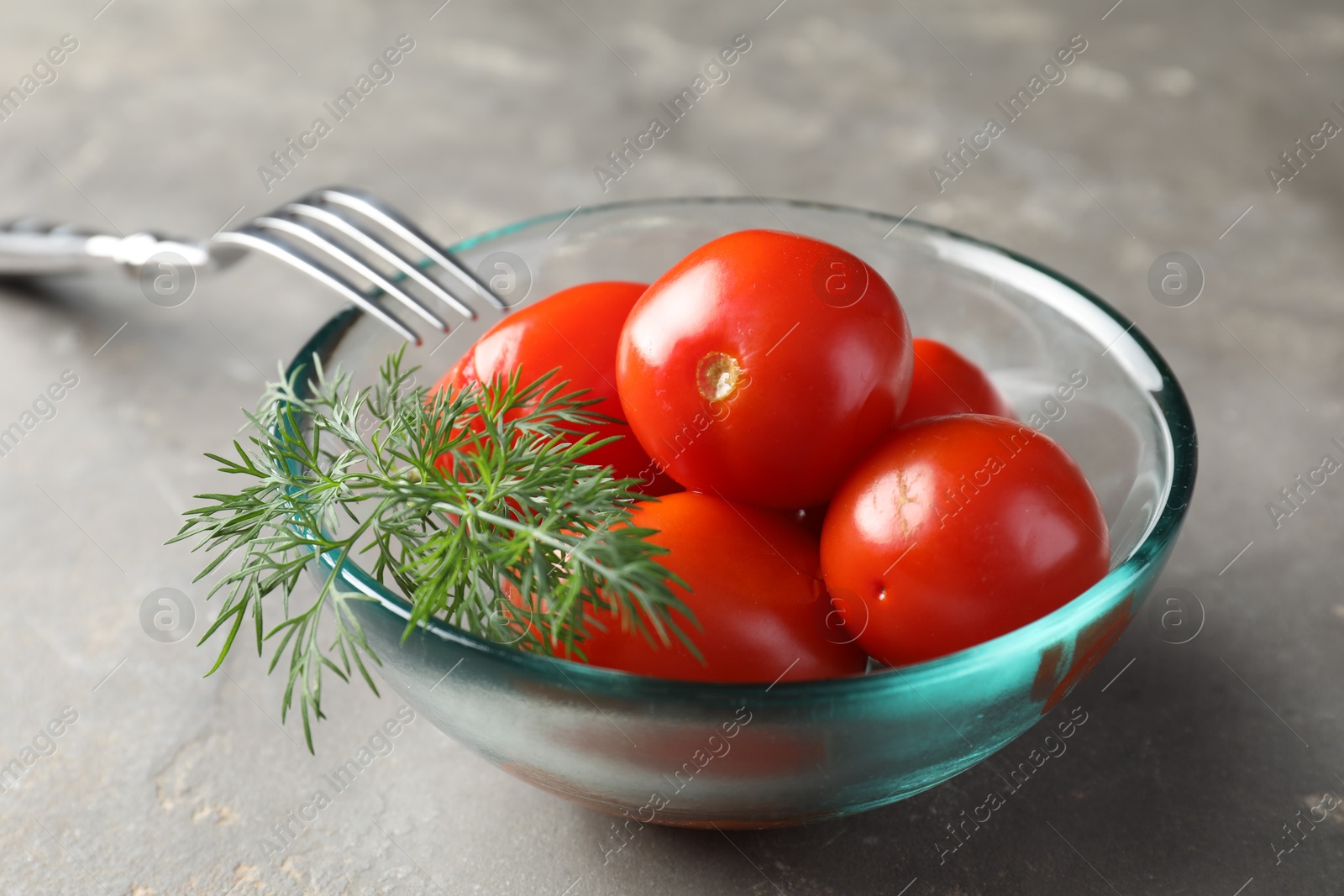 Photo of Tasty pickled tomatoes in bowl, dill and fork on grey table