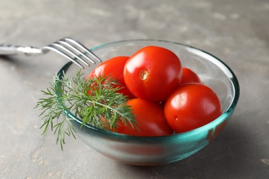 Photo of Tasty pickled tomatoes in bowl, dill and fork on grey table