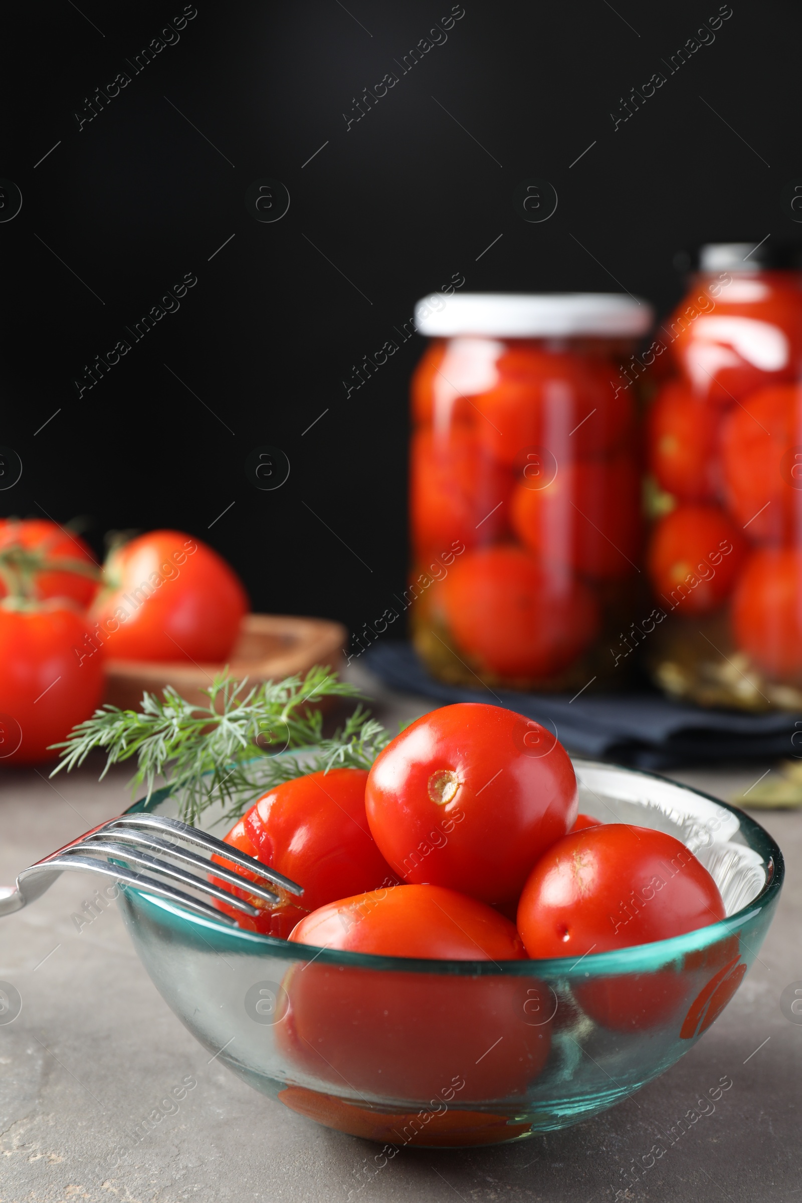 Photo of Tasty pickled tomatoes in bowl, fresh vegetables, dill and fork on grey table