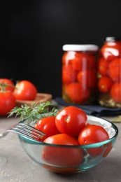 Photo of Tasty pickled tomatoes in bowl, fresh vegetables, dill and fork on grey table
