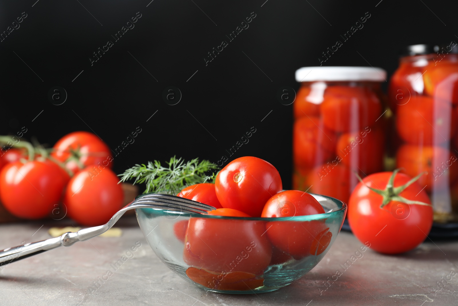 Photo of Tasty pickled tomatoes in bowl, fresh vegetables, dill and fork on grey table