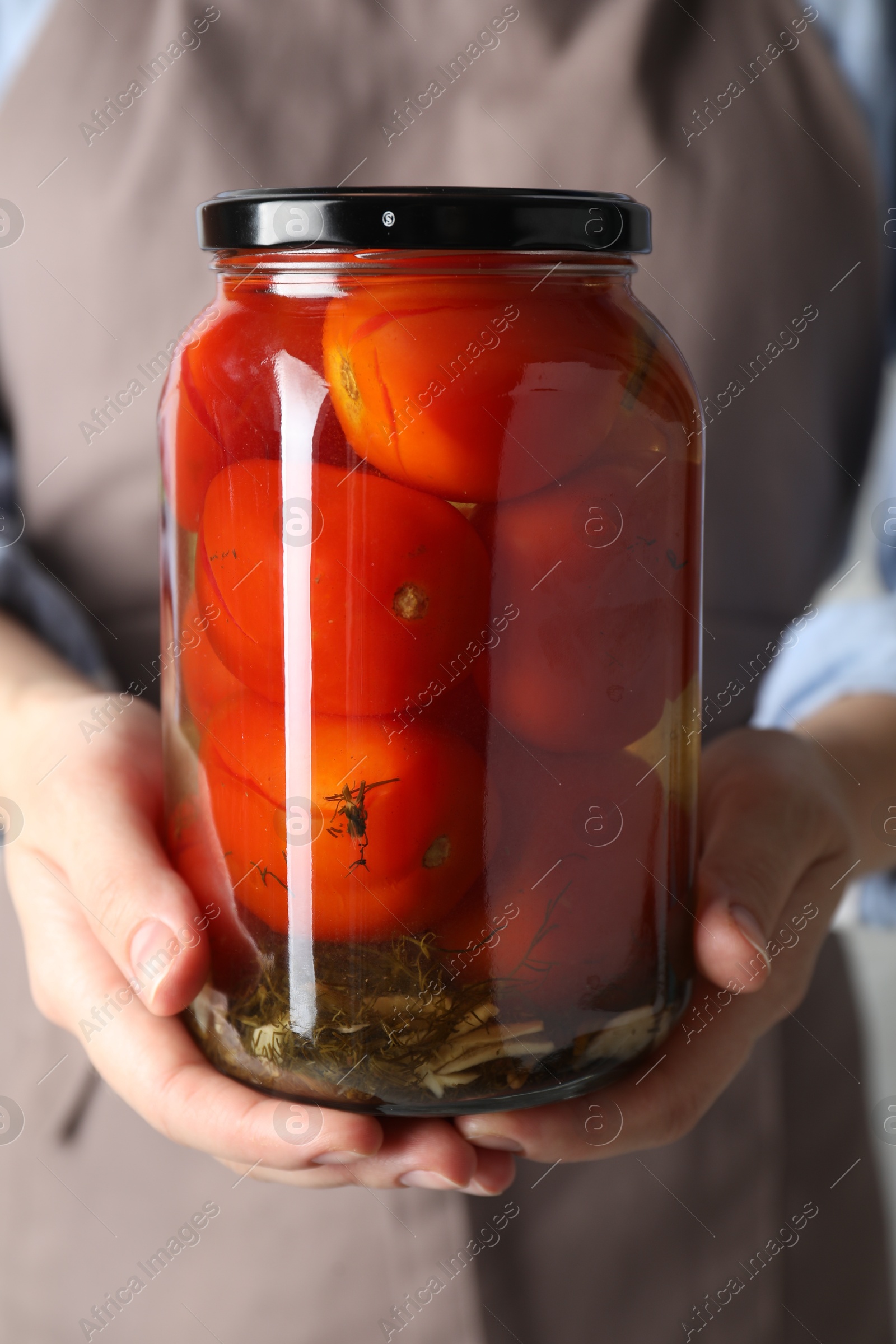 Photo of Woman holding jar with tasty pickled tomatoes, closeup